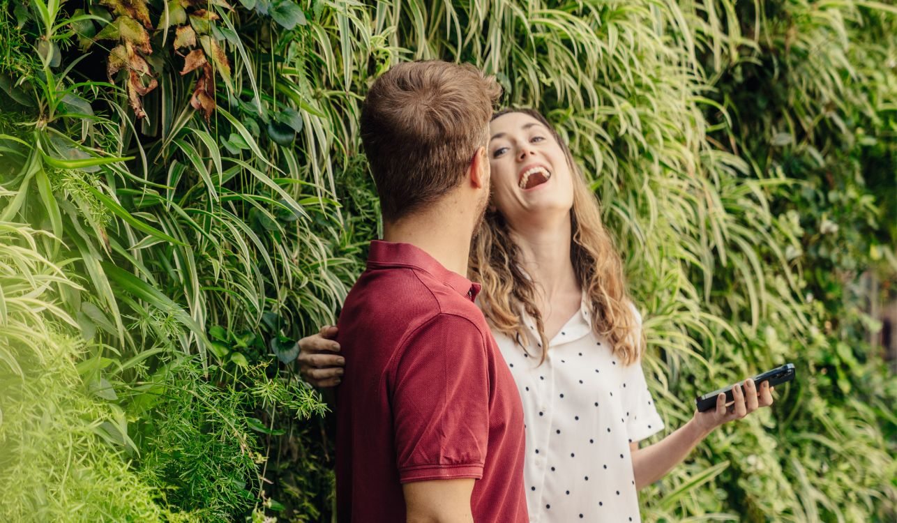 Pessoas sorrindo e conversando com jardim vertical ao fundo.